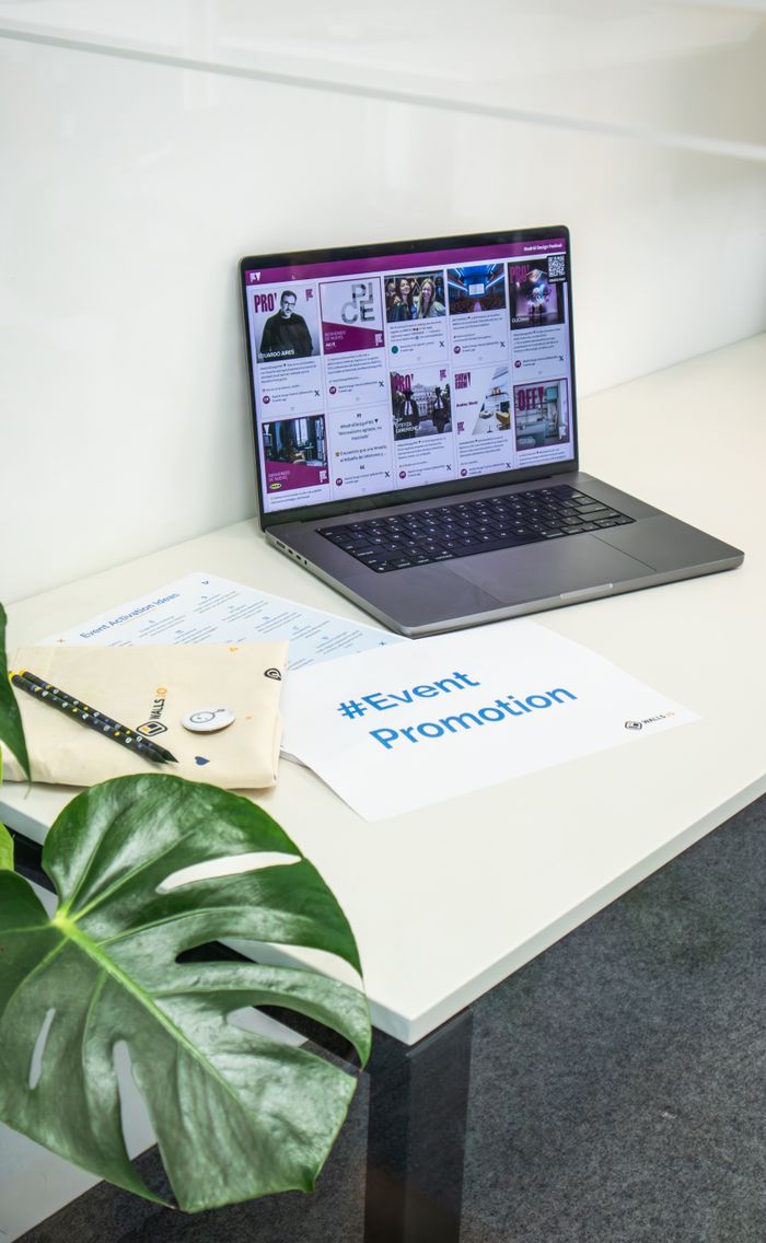 Espace de bureau épuré avec un ordinateur portable affichant les réseaux sociaux, des papiers et une plante pour la promotion d’un événement.